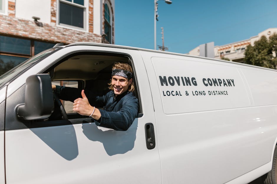 Two men from Man with Van Coulsdon are engaged in the home relocation process, depicted loading or unloading a large cardboard box from a white delivery van parked on a brick driveway. The van's rear 